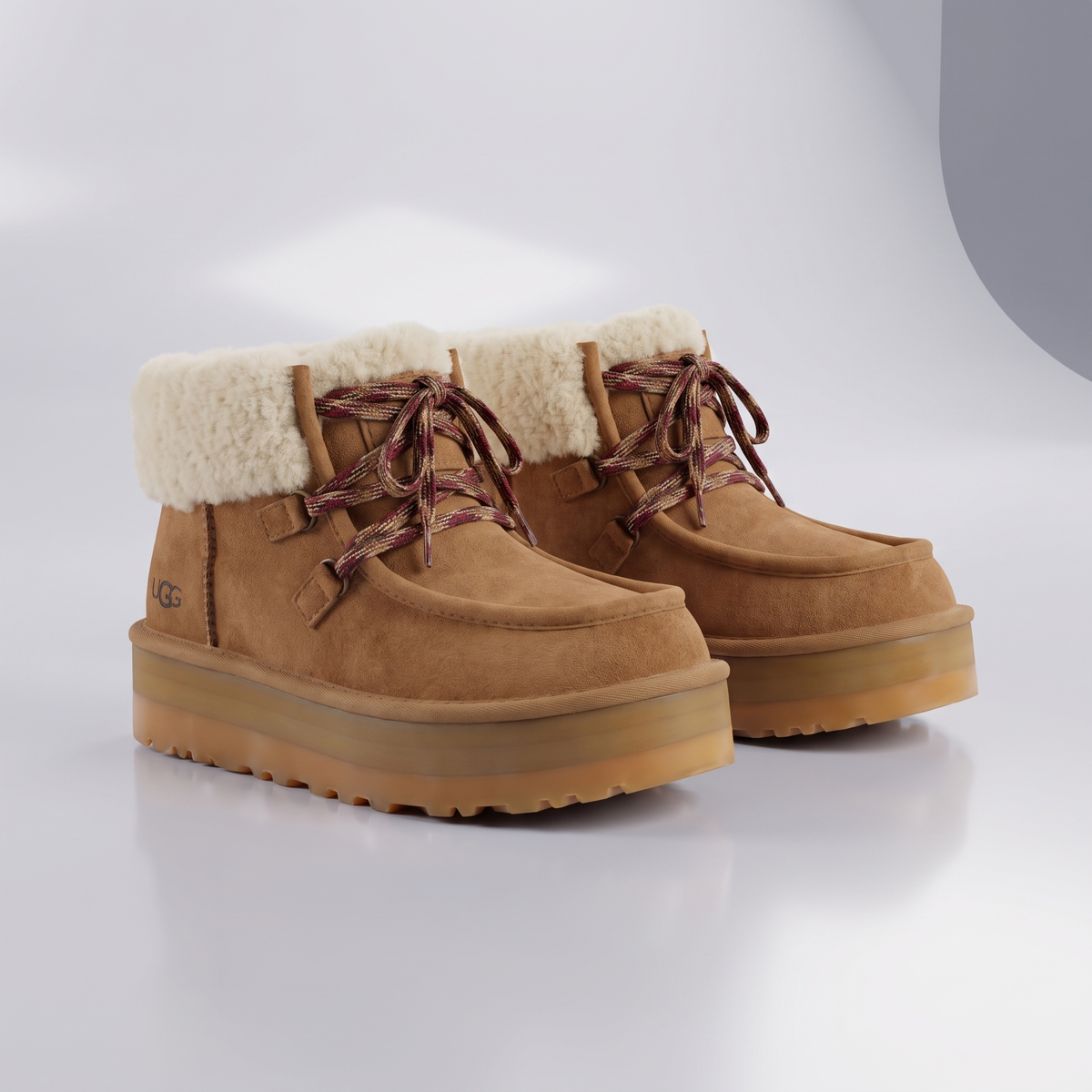 A pair of UGG mid-calf boots in tan suede with a cream shearling lining, brown laces, and a chunky gum sole, shown on a clean white studio background.