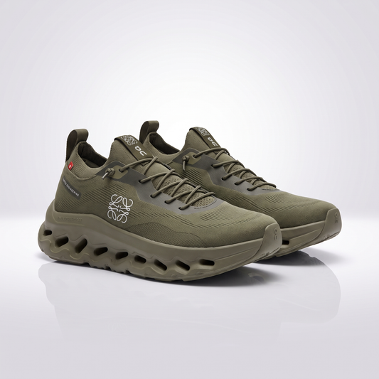 A pair of olive green running shoes with a chunky, sculpted sole featuring circular cutouts, displayed on a clean white reflective studio surface.